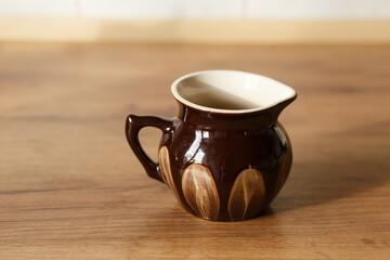Classic glazed ceramic jug with hand-painted natural motif, standing on wooden surface, country-style tableware or vintage home decor