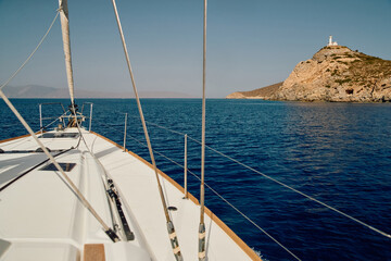 view from a sailing boat to an island with a lighthouse in clear sunny weather, the bow of the...