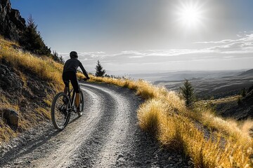 Person cycling uphill on a winding gravel mountain road under bright sunlight with scenic valley and distant mountains in the background