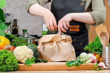 Chef puts vegetables peels in paper container processing compost. Wooden table, kitchenware, vegetables, herbs and ingredients. Healthy eating, zero waste, blogging, recycling
