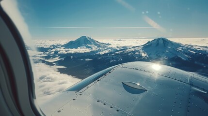 Snow-capped mountains peek through thin clouds as the morning sun glistens on the aircraft wing under a vast, clear blue sky.