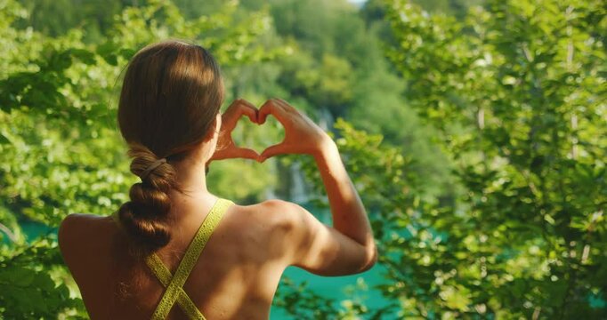 Woman making heart shape with hands while looking at lush nature of Plitvice Lakes in Croatia
