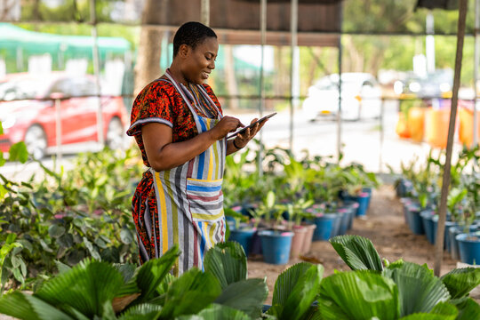 Successful African female horticulturist taking inventory of plants in her garden with her smart tablet, recording orders and talking to customers remotely.