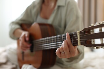 Young woman playing guitar at home, closeup