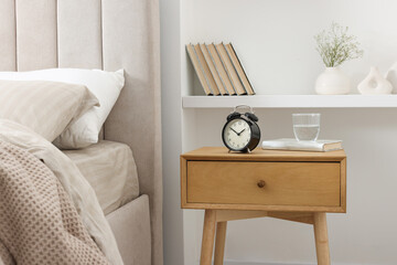 Bedside table with alarm clock, glass of water and book near bed indoors