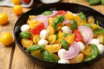 Tasty salad with yellow tomatoes, basil, onion and mozzarella cheese on wooden table, closeup
