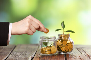 Investment concept. Woman putting coin into glass jar at wooden table against blurred green...