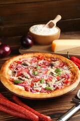 Tasty pizza with smoked sausages and ingredients on wooden table, closeup