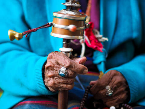 Close-up of aged hands holding a Tibetan prayer wheel and beads, symbolizing spirituality and tradition