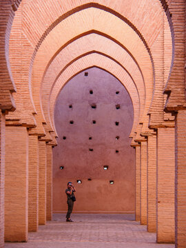 Tourist takes photo inside arched corridor with intricate Islamic brick architecture and warm light 12th Century Mosque in the High Atlas Mountains - UNESCO World Heritage Site.