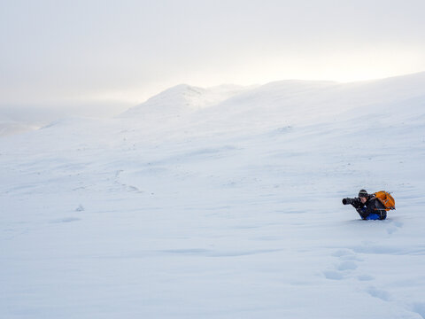 Photographer lying in snow on arctic mountain slope, copy space