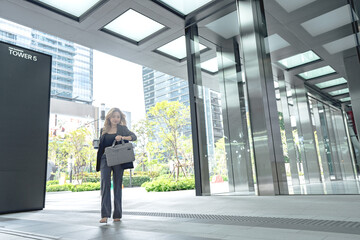 professional woman working indoor lobby, surrounded by lush greenery and city skyscrapers. female holdign coffee for morning work.