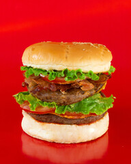 Double-meat burger with vegetables in the foreground with a red background