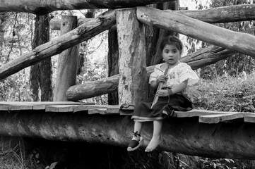 Indigenous girl sitting on wooden bridge in forest holding plant