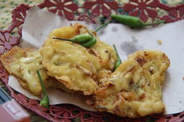 Close-up of Indonesian fried snacks called “bakwan” or vegetable fritters, served with green chilies on a traditional red tray lined with paper. A popular savory street food in Indonesia.