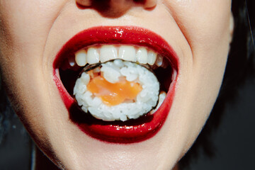 Close-up portrait of a woman enjoying sushi with vibrant red lipstick and a playful expression,...