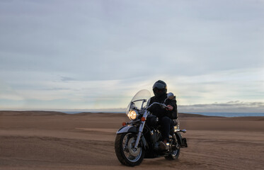Man on motorcycle in desert during sunset with dramatic clouds — concept of freedom, travel, solitude, adventure, and outdoor lifestyle in wild open landscapes