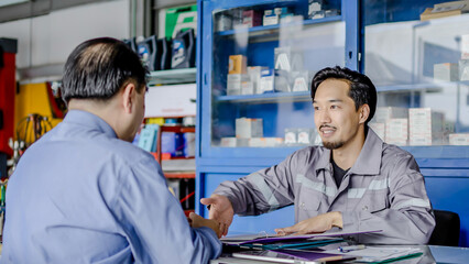 Obraz premium Professional vehicle maintenance man holding clipboard and talk with asian man customer at car service garage. Car repair and customer service concept, Discussing the cost of car repairs at the desk
