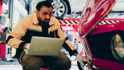 Mechanic Asian man using computer laptop examining tuning fixing repairing front car engine automobile vehicle parts using tools equipment in workshop garage support and service in work uniform