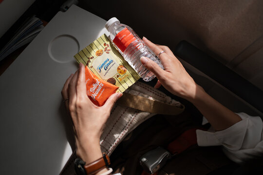 BANGKOK, THAILAND - JUN 25, 2024: Passenger holding snacks from Firefly, a bottle of water, packet of salted peanuts, and Famous Amos cookies on an airplane tray table during in-flight snack service