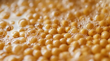 Close-up of fresh soybeans being soaked in water, with bubbles forming on the surface. The golden beans contrast with the clear liquid, capturing the first step in traditional tofu-making.