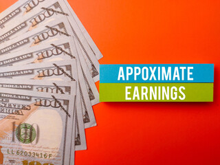 Top view sticky note and banknotes with the word APPOXIMATE EARNINGS on a orange background