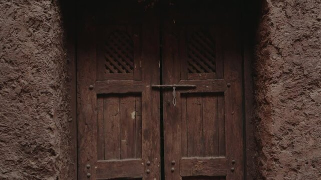 Old wooden door in a traditional Moroccan house. The rustic texture of the mud walls and the weathered wood creates a sense of history and timelessness.