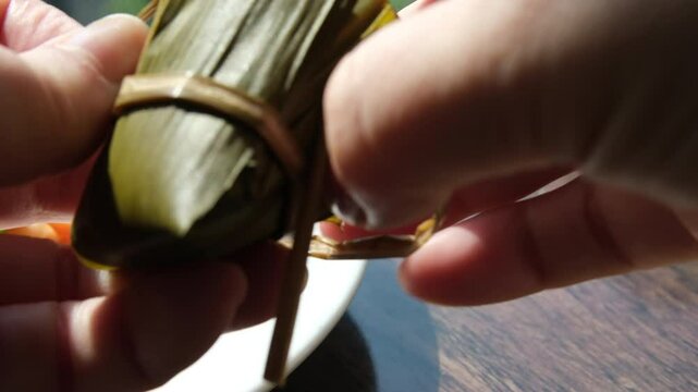 Hand holding zongzi rice dumpling with savoury fillings wrapped in bamboo or reed leaves.