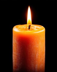 Close up of a burning orange candle against a black background creating a warm glow in a studio setting