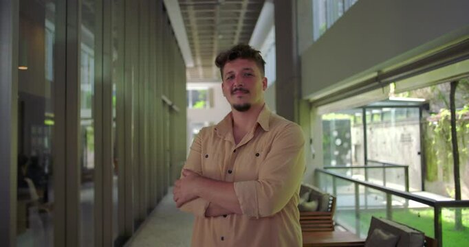 Man standing in office hallway with arms crossed, confident expression, assertive posture in modern workplace, strength and leadership presence
