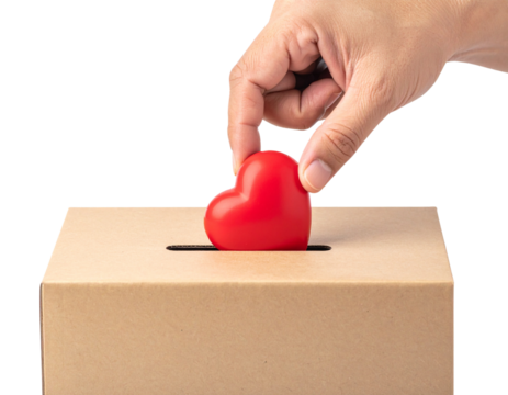A hand drops a red heart into a cardboard donation box, symbolizing charity and giving.