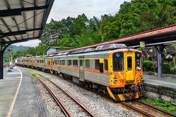 Obraz premium Local passenger train waits at the platform of Shifen Station, nestled in the lush green hills of New Taipei, Taiwan. The scenic station is part of the historic Pingxi Line, popular with tourists for