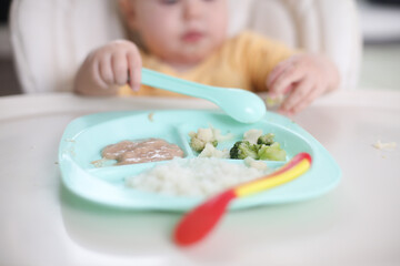 Cute little baby eats food from a plate at a table