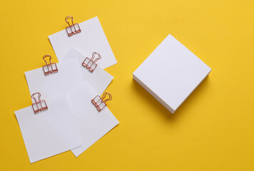 Memo white square sheets of paper with binder clips on yellow background. Stationery, education,...