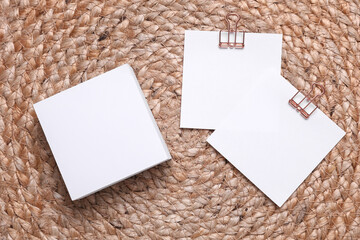 Memo white square sheets of paper with binder clips on straw mat. Stationery, education, business...