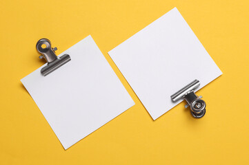 Memo white square sheets of paper with binder clips on yellow background. Stationery, education,...