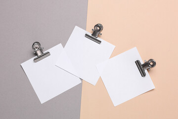 Memo white square sheets of paper with binder clips on pastel background. Stationery, education,...