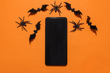 Smartphone with halloween bats and spiders on orange background