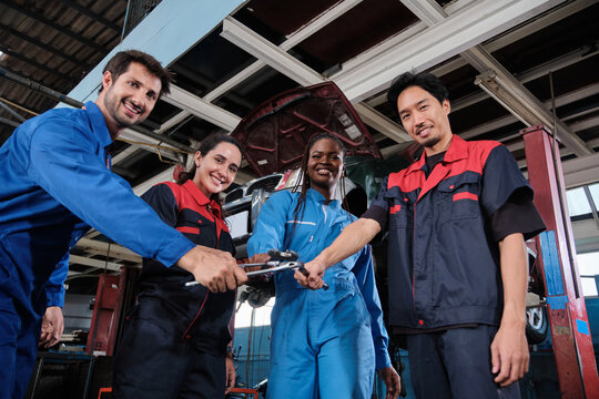 Harmonious professional mechanic teamwork, multiracial engineers with wrenches united, cheerful, and happy smile in fix car garage, maintenance service jobs in automotive transport industry station.