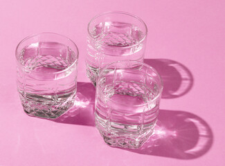 Glasses of water with reflection and shadow on pink background. Minimalism.