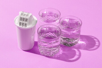 Cartridge filter for filtering water and glasses of clean water on pink background with shadow....