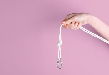 Female hand holds rope with carabiner on pink background. Mountaineering, active recreation