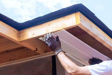 Skilled worker places plastic soffit material in eaves of house while working outdoors.