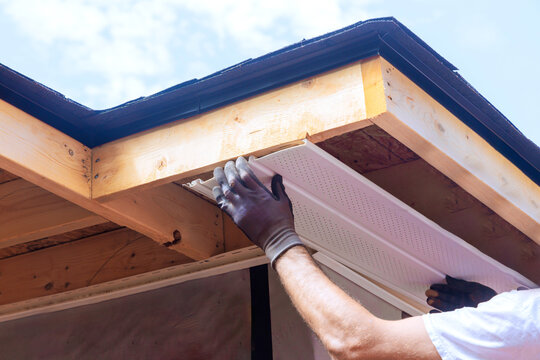 Skilled worker places plastic soffit material in eaves of house while working outdoors.