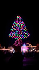 Person holding a vibrant multicolored Christmas tree light decoration against a dark background at night.