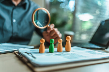 Fototapeta premium The wooden doll represents the employee of the company and Human Resource use magnifying glass view them on document in workplace. Search or find new job and Corporation, Enterprise concept.