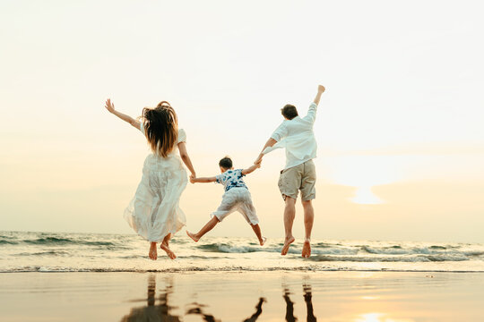 Family jumping happily with their hands raised, having fun on the beach with family during a holiday, travel, long weekend, summer or any other holiday. They are happy to spend time together.