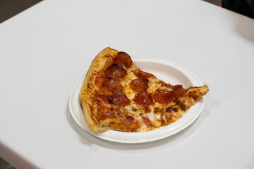 A slice of pepperoni pizza on the table at a food court.