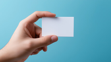 Fototapeta premium Hand holding a blank white business card against a blue background. 