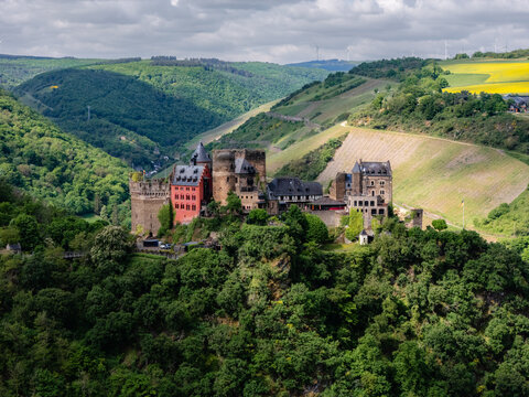 Aerial view of Sch&ouml;nburg Castle, a medieval fortress and hotel near Oberwesel, Germany. Set in the UNESCO Upper Middle Rhine Valley, surrounded by forests and vineyards, with distant wind turbines.